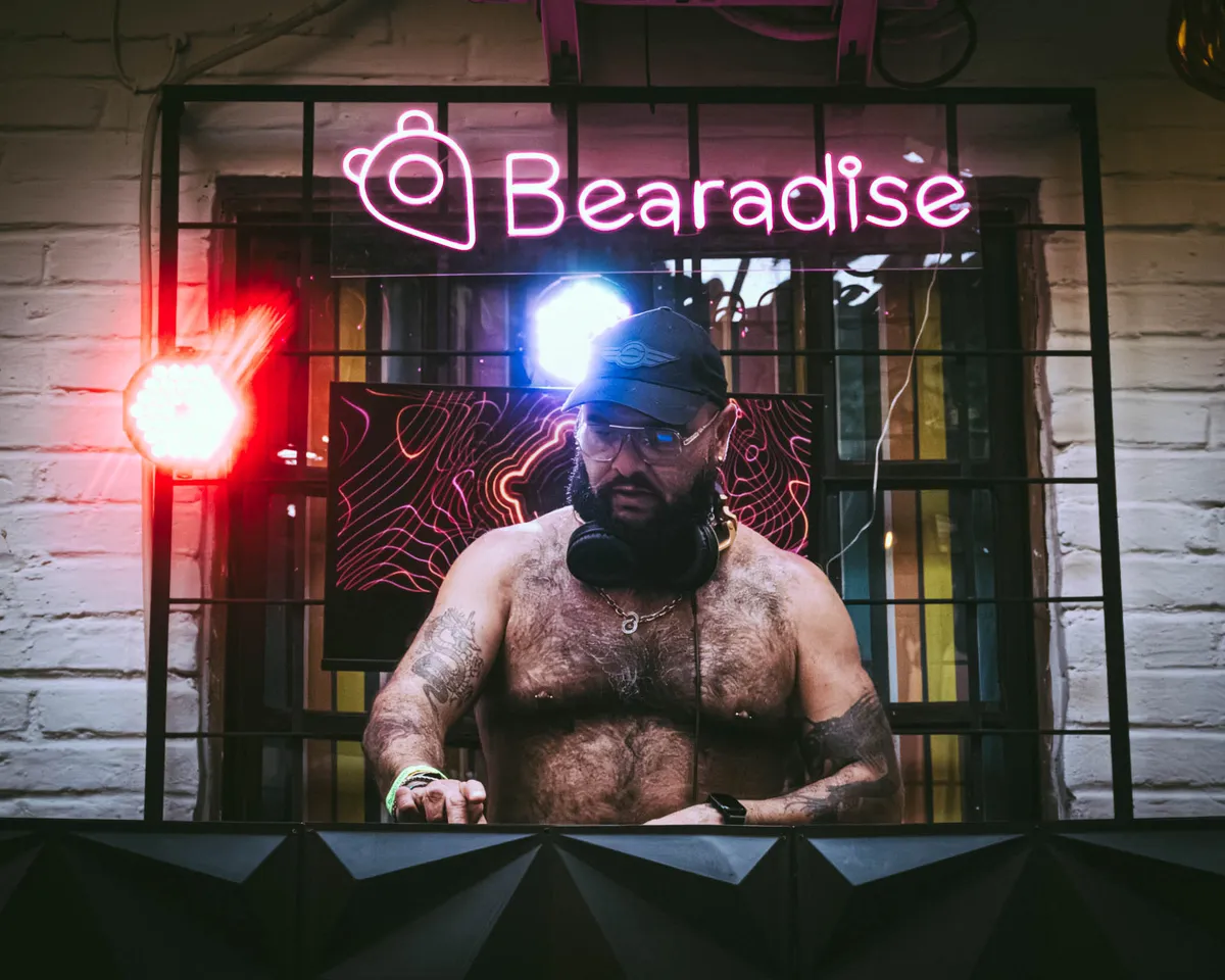 A DJ at the decks under a pink neon Bearadise sign