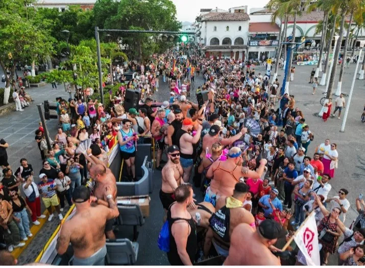 Our double decker bus in the Vallarta Pride parade, guests waving from the top deck over a packed crowd