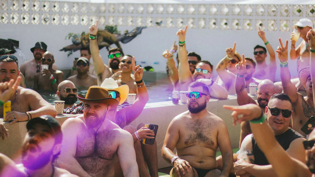 A pool party crowd in cowboy hats and sunglasses with their hands in the air
